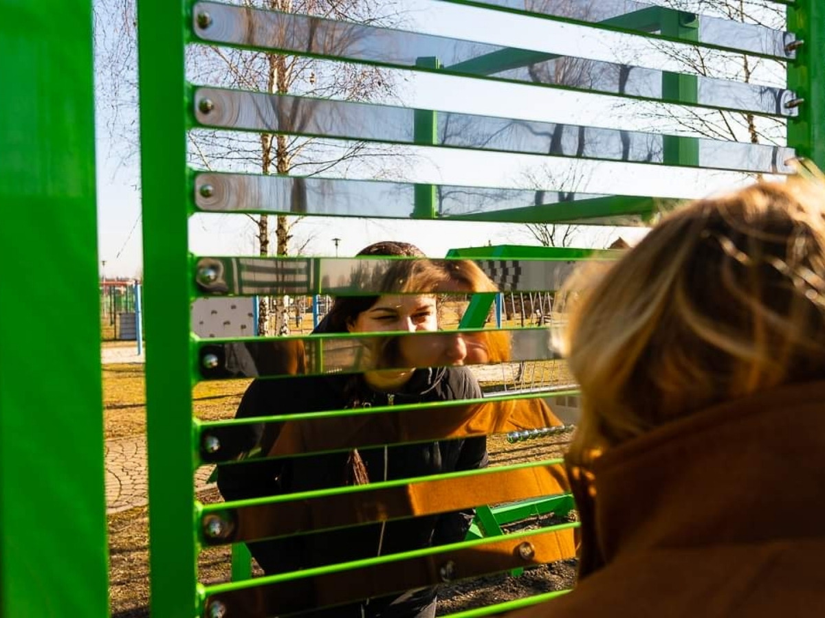 Wąska szpara między dwiema lustrzanymi listwami, przez którą widać oko dziecka stojącego po drugiej stronie ściany
