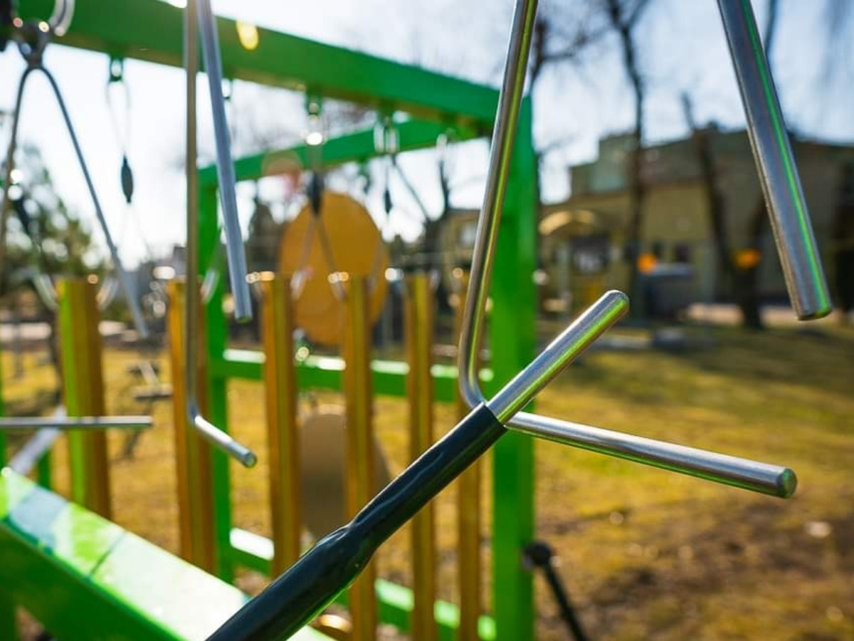 Steel triangle hanging on a cable in the green frame of the musical panel, with a child's hand holding a beater beside it