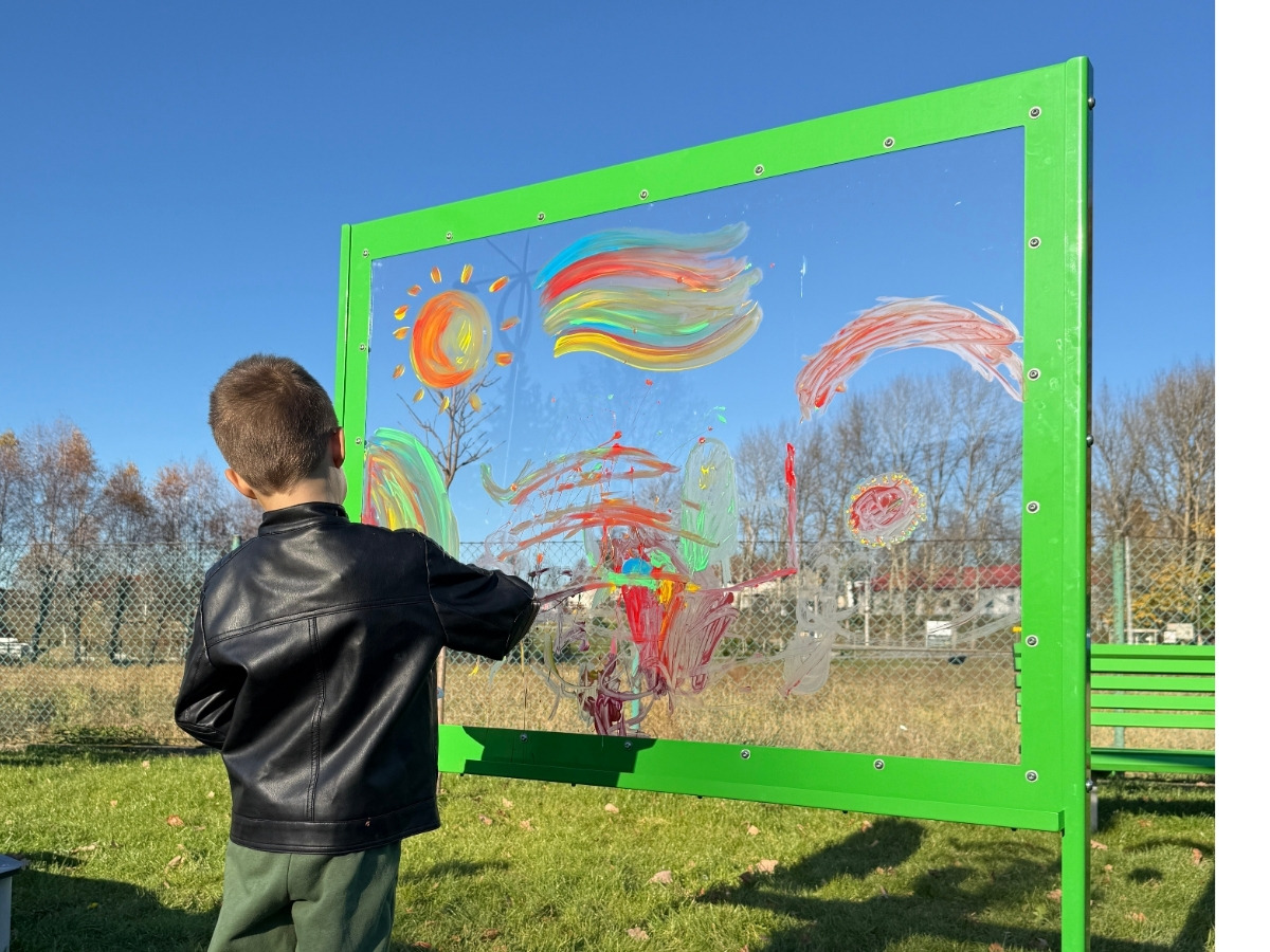 A child tracing with a brush on the transparent panel the outline of another child standing still on the opposite side