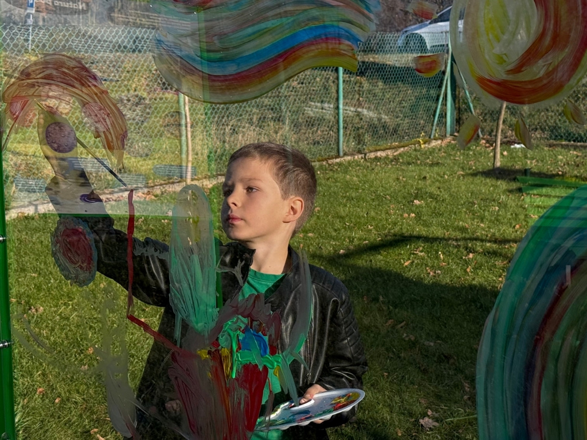 A child's hand wiping the transparent panel with a damp cloth, colourful paint coming off the surface in streaks