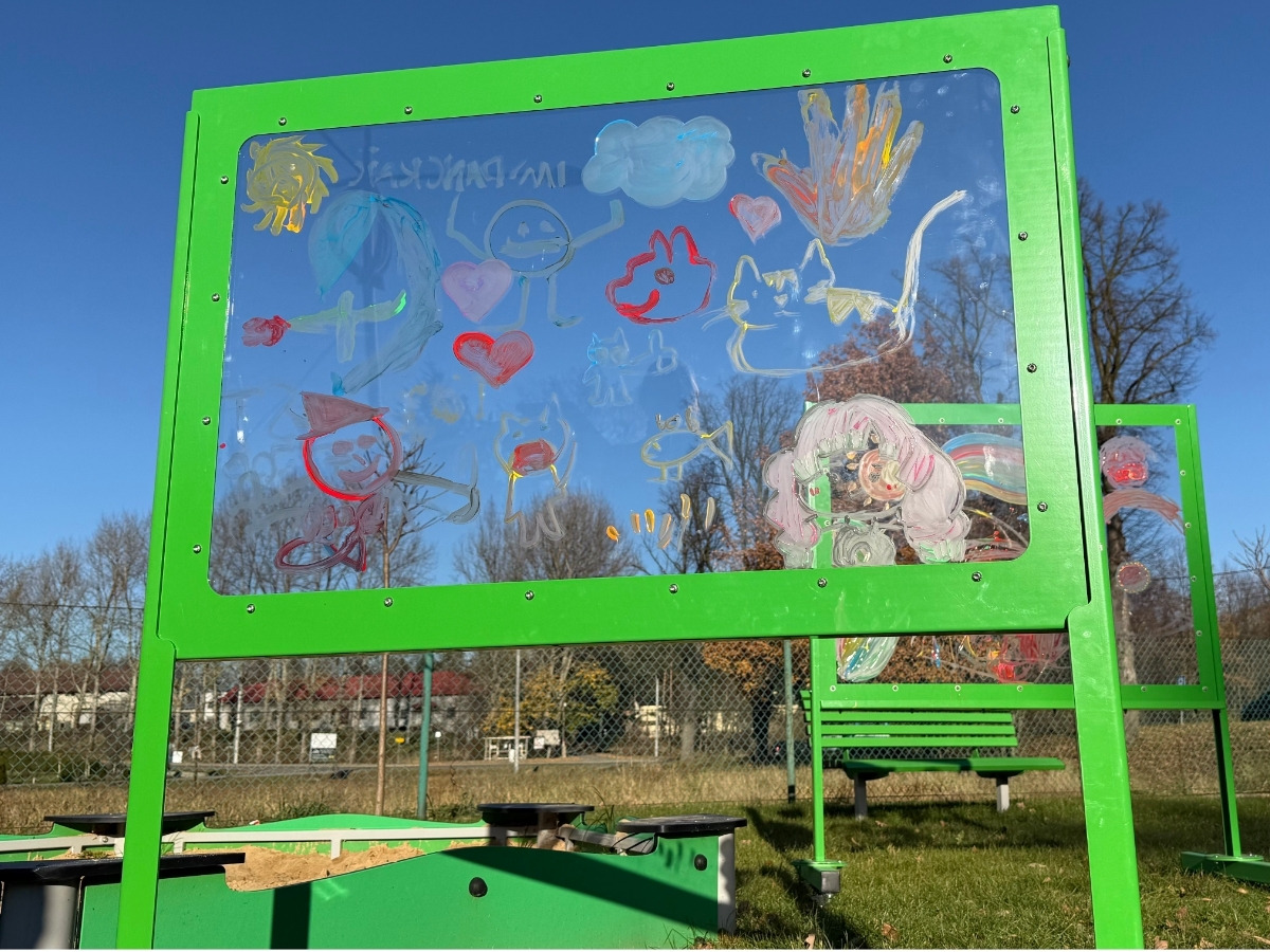 The whole painting wall, side view: a transparent panel set in a green steel frame, with a child standing beside it