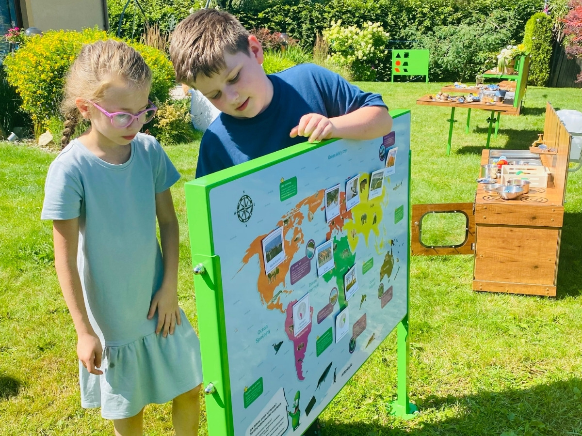 Dwustronna tablica edukacyjna w&nbsp;jednej ramie, dzieci stoją po obu stronach planszy
