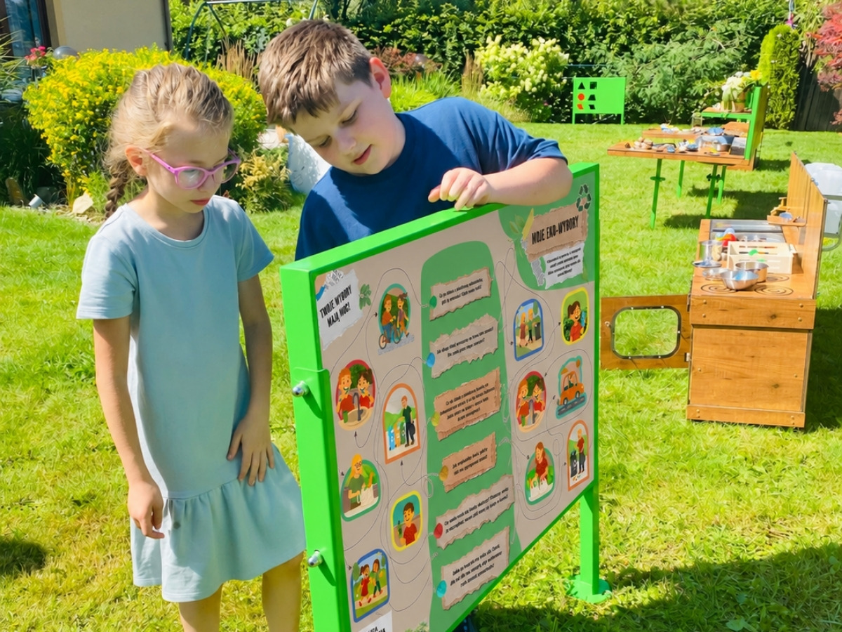 Dwustronna tablica edukacyjna w&nbsp;jednej ramie, dzieci stoją po obu stronach planszy
