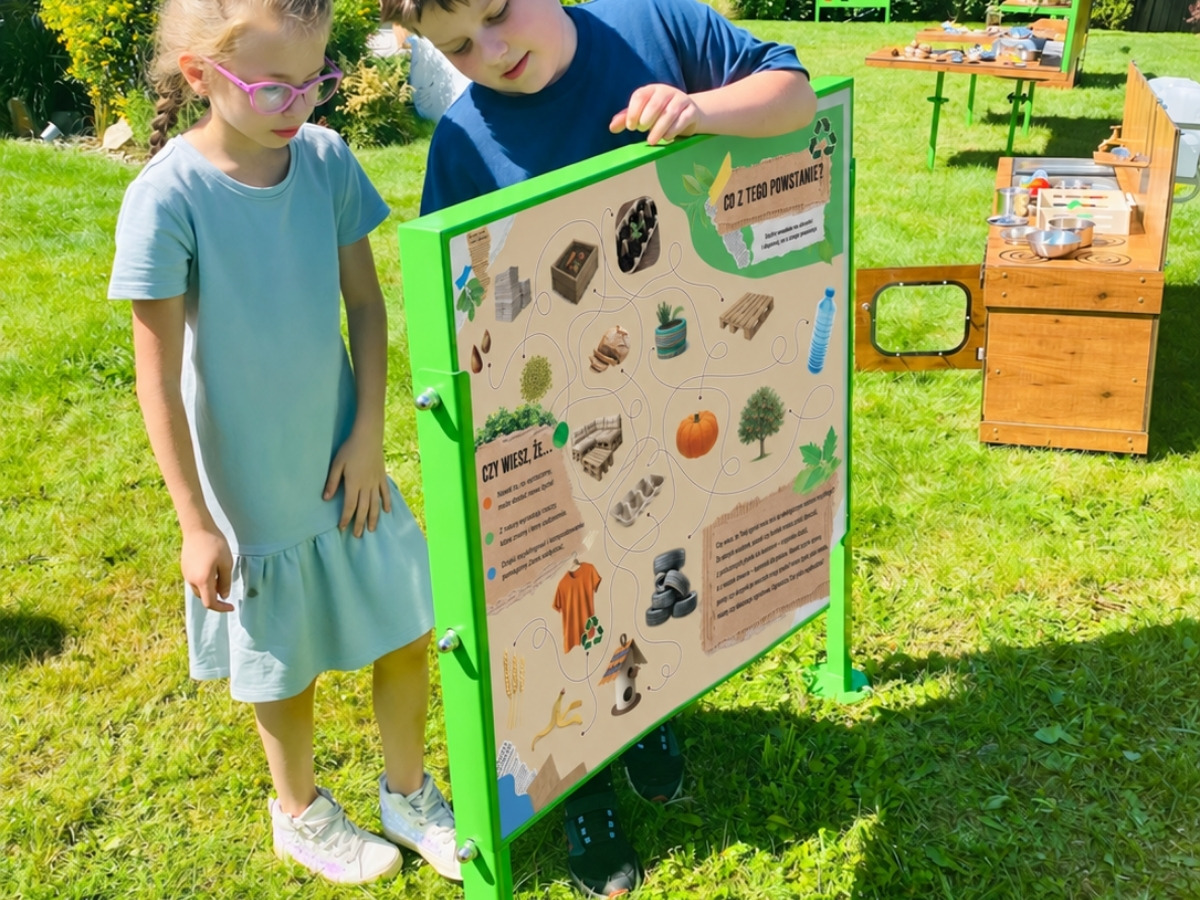 Dwustronna tablica edukacyjna w&nbsp;jednej ramie, dzieci stoją po obu stronach planszy
