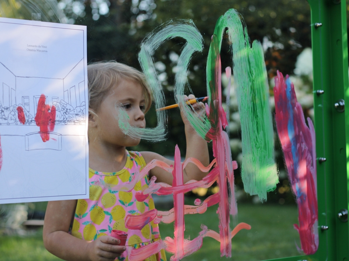 Two children painting at the same time on either side of the Picasso board, both drawings visible on the pane at once