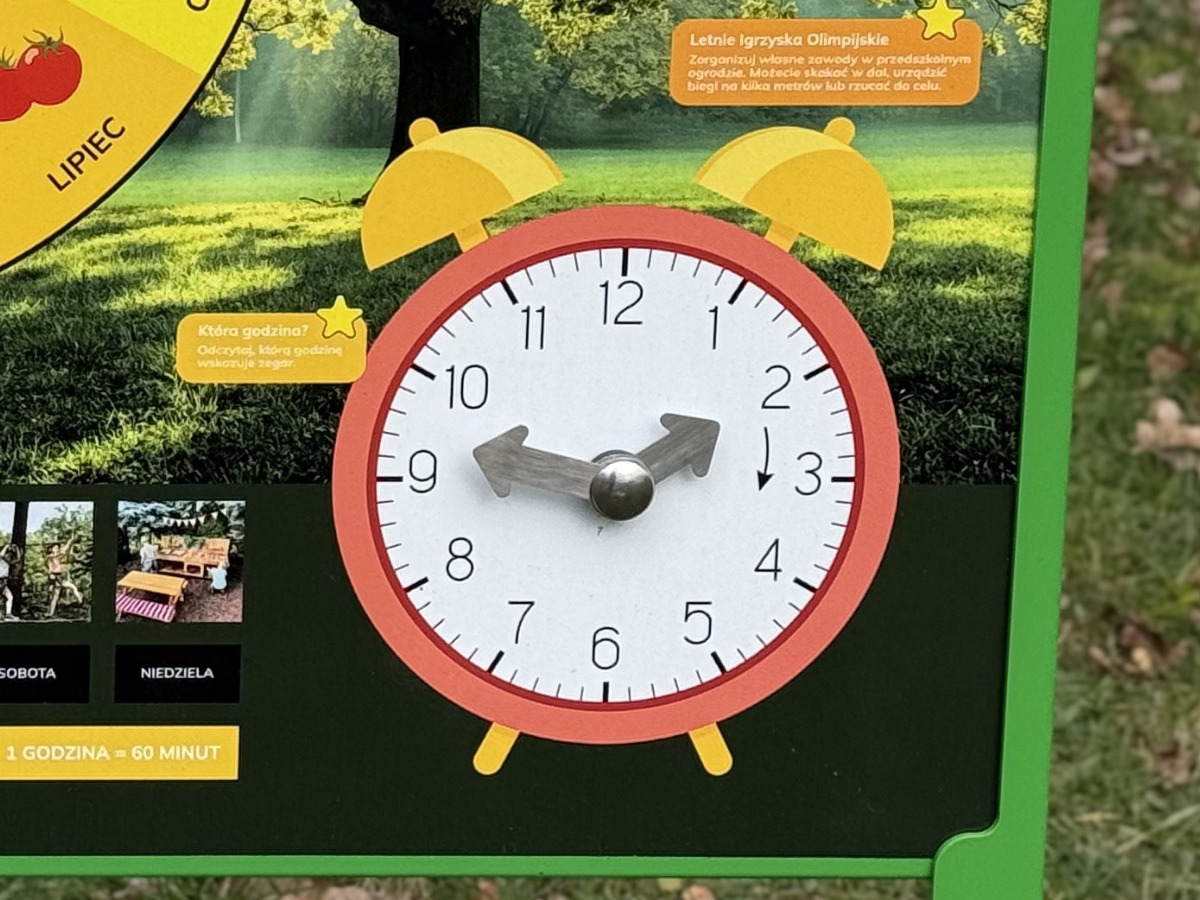 Clock face on the S13 Educational Board - 4 Seasons with two metal hands, a child's hand moving the hour hand