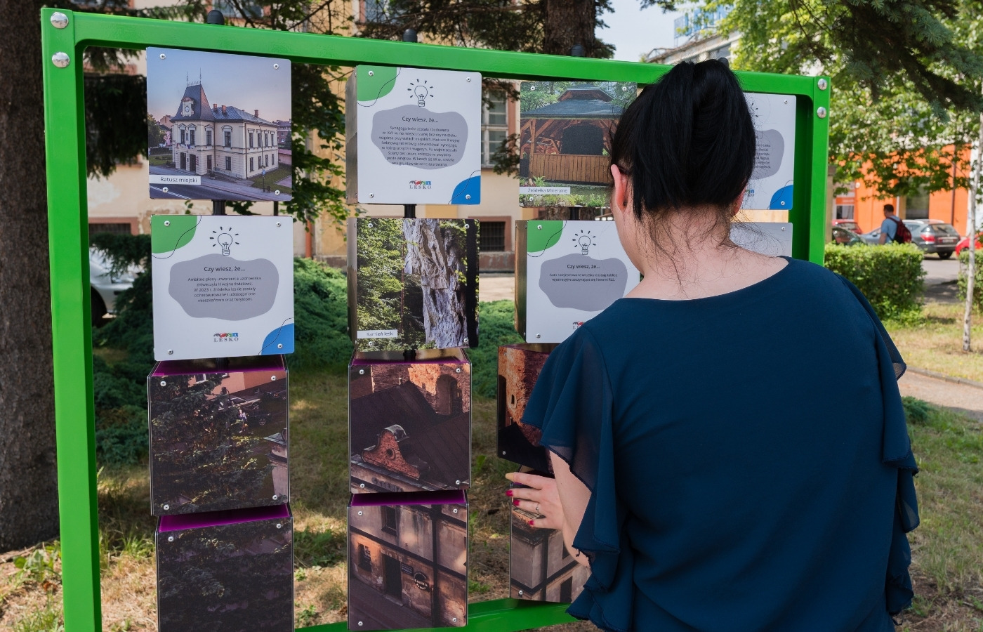 Kobieta przy tablicy memory w&nbsp;zielonej ramie w&nbsp;parku miejskim, urządzeniu, które można sfinansować z&nbsp;budżetu obywatelskiego