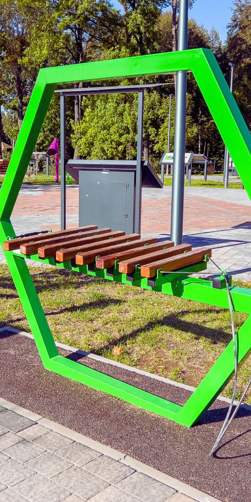 Muzyczny plac zabaw w parku: ksylofon z drewnianymi sztabkami w zielonej sześciokątnej ramie